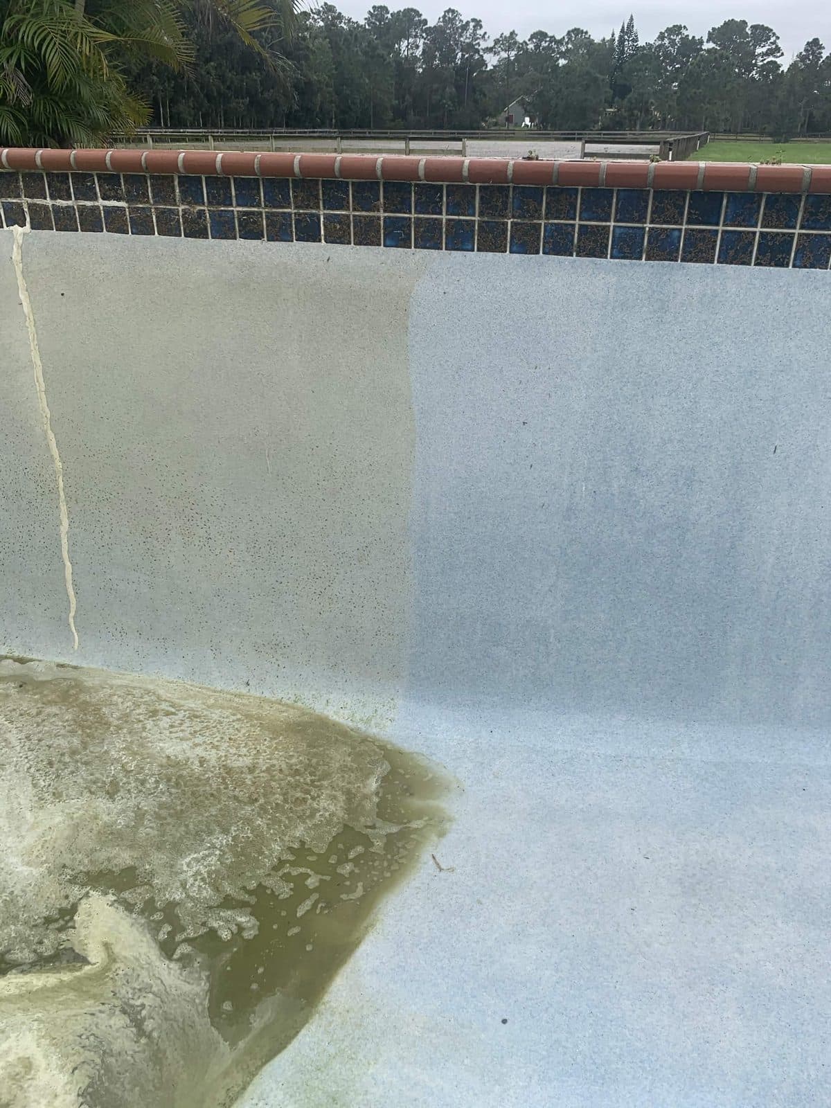 Acid wash underway on a pool wall, one stripped clean panel beside the untreated stained plaster