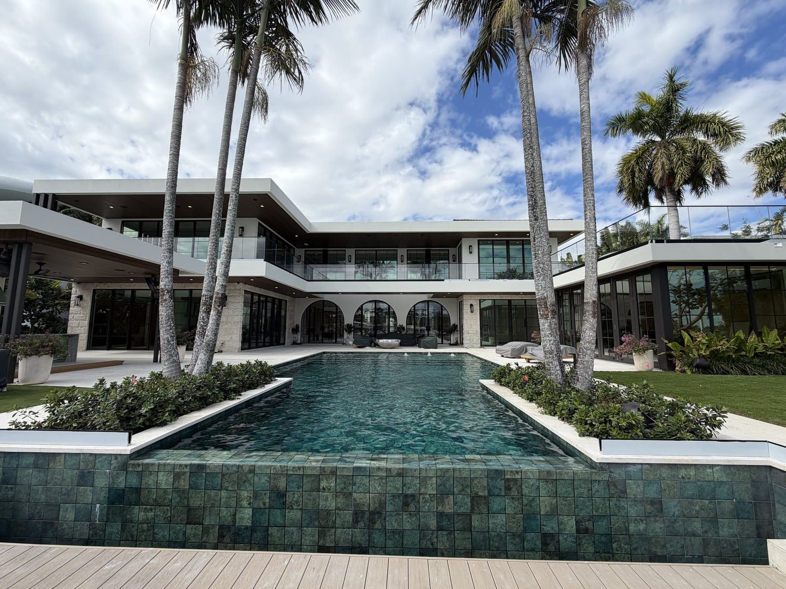Long rectangular pool with dark green glass tile and a raised spa wall behind a modern two storey waterfront home in Wellington FL